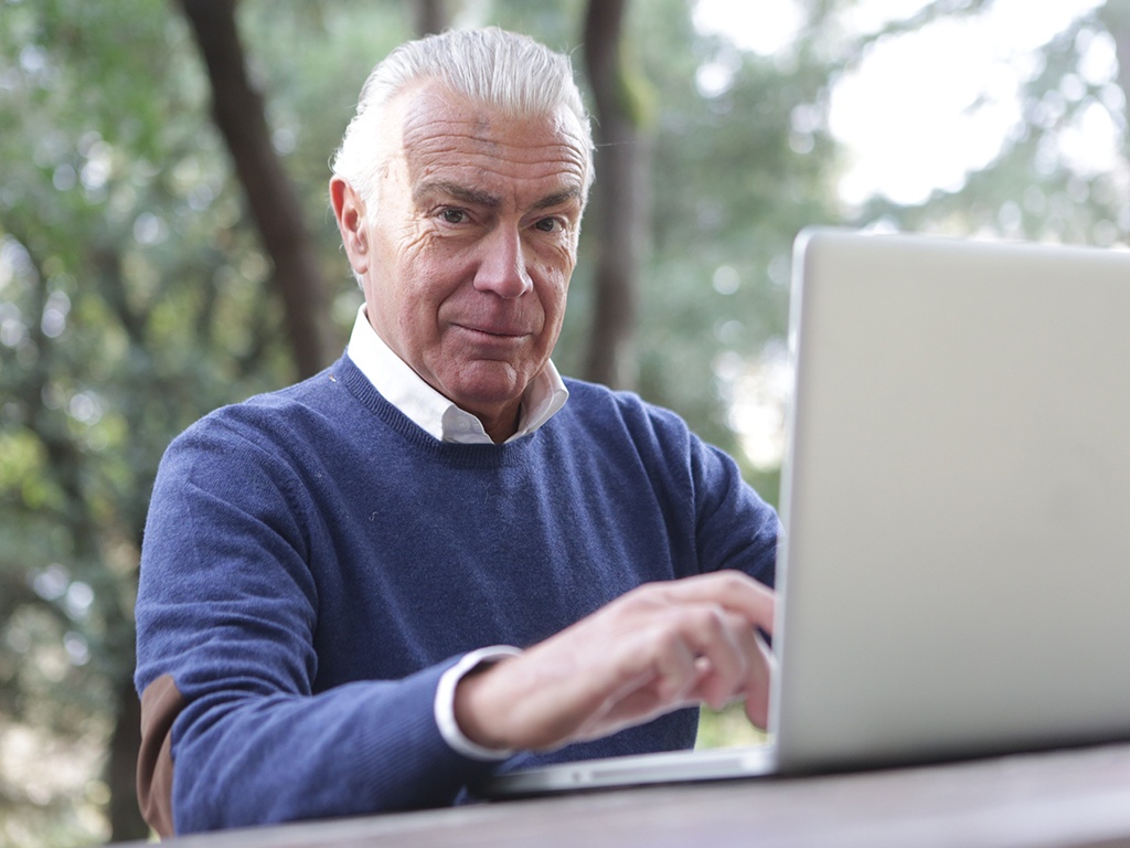 Ein Best-Ager sitzt an seinem Laptop unter freiem Himmel