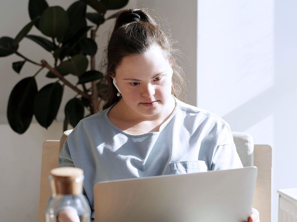 Junge Frau mit Down-Syndrom arbeitet am Laptop.