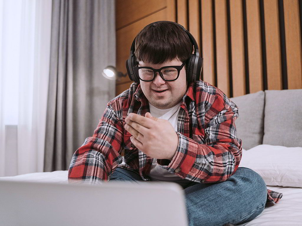 Junger Mann mit Down-Syndrom sitzt mit Kopfhörern am Laptop.